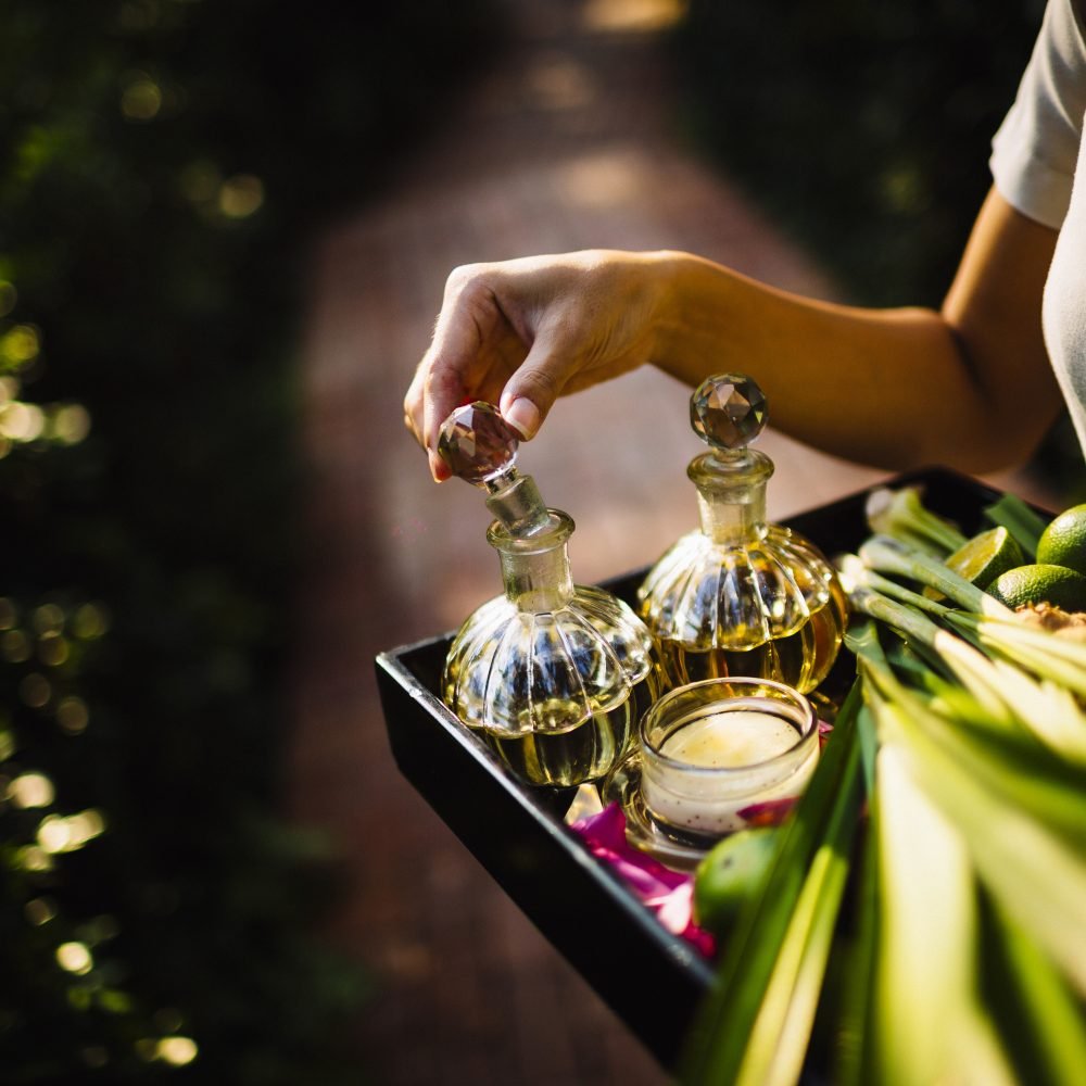 High angle close up of woman holding tray with glass bottles, candles and fruit.